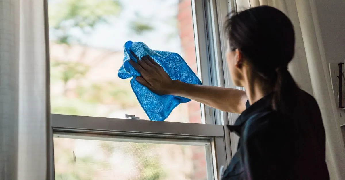 A woman cleans a window using a blue microfiber cloth providing a streak-free shine.
